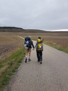 Dois peregrinos de mochila caminhando lado a lado numa estrada