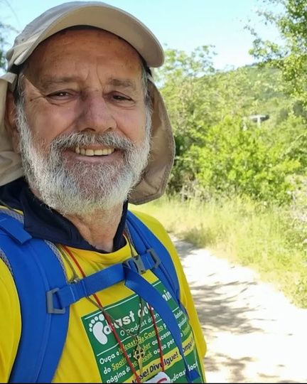 Hélio Araújo sorrindo, de chapéu e mochila, numa trilha
